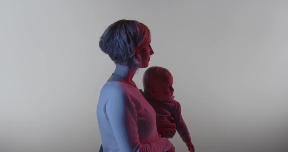 A woman is holding a baby and staring into the distance