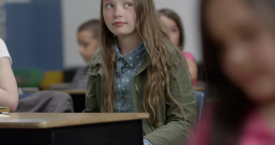 A young girl puts a folder in her desk and raises her hand