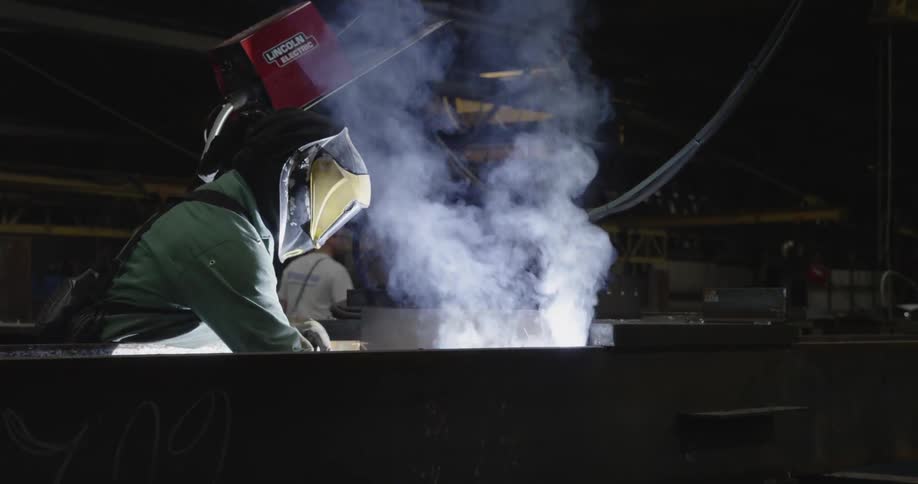 A man welds a large steel beam in a warehouse