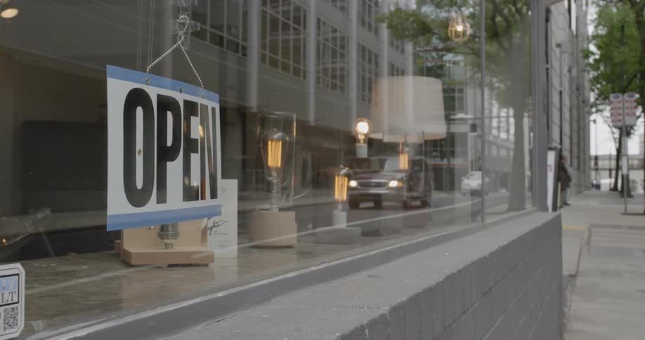 A person is flipping a sign to 'open' in a cafe in a city during the day