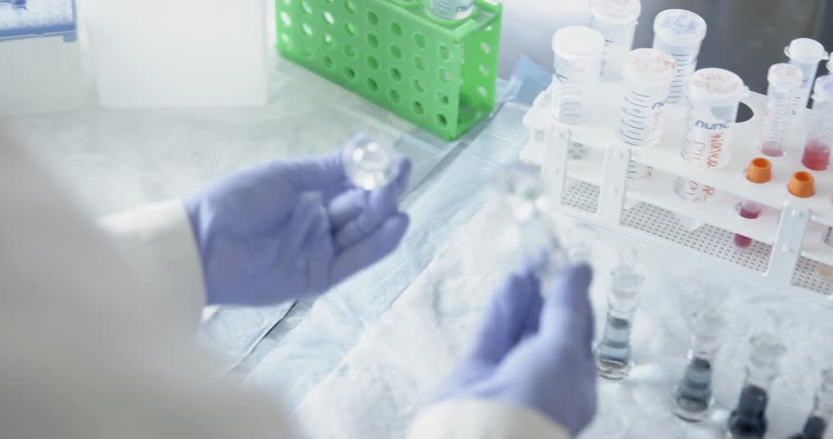 A technician in a lab is picking up and mixing liquids in vials in daylight