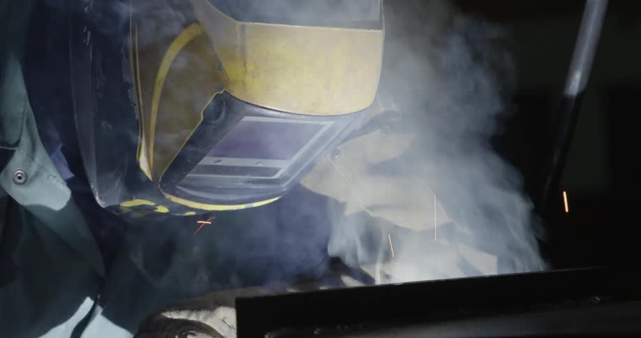 A man welds a large steel beam in a warehouse