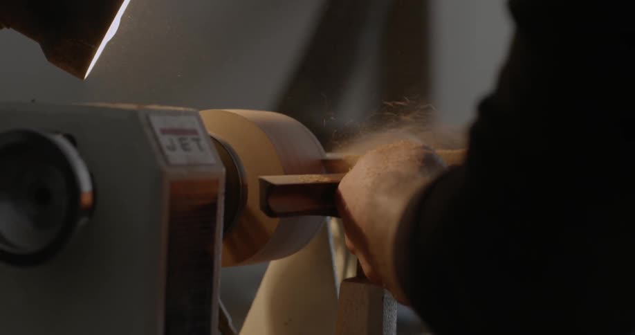 A man is sanding down a piece of wood on a lathe