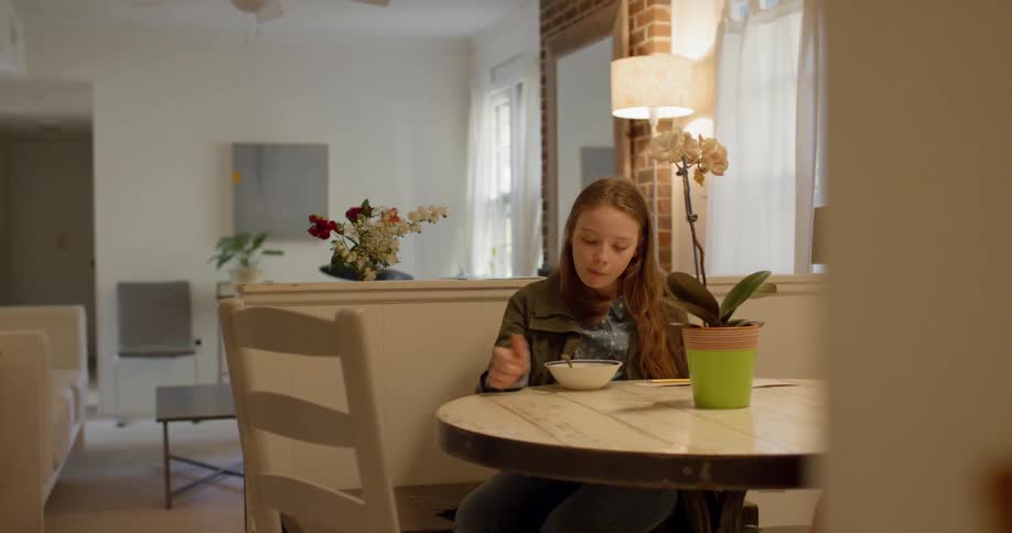 A young girl eats cereal and then stands up at a dining table