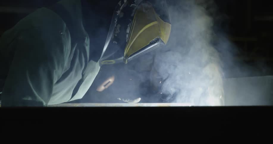 A man welds a large steel beam in a warehouse