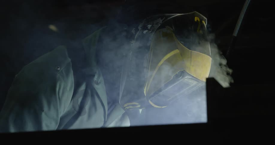 Someone is wearing a welders mask and they are welding in a factory