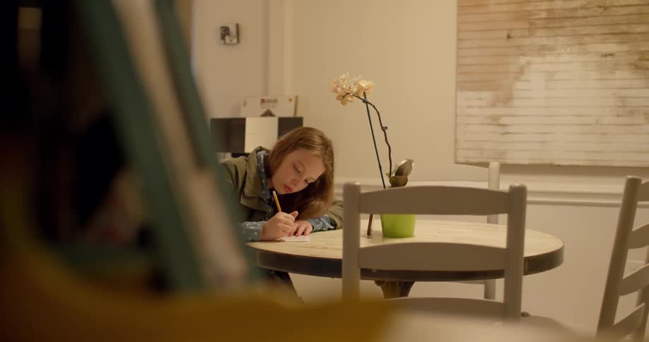 A girl writes on a piece of paper at a table