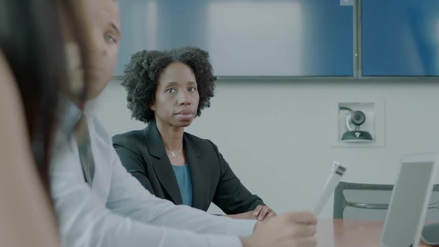 A woman is working with others at a conference table in an office during the day