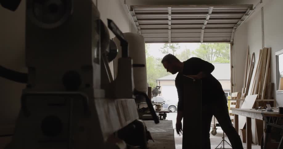 A man wipes down a piece of wood in a garage