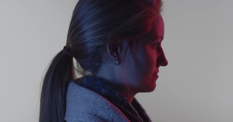 A woman stares blankly in a dark room