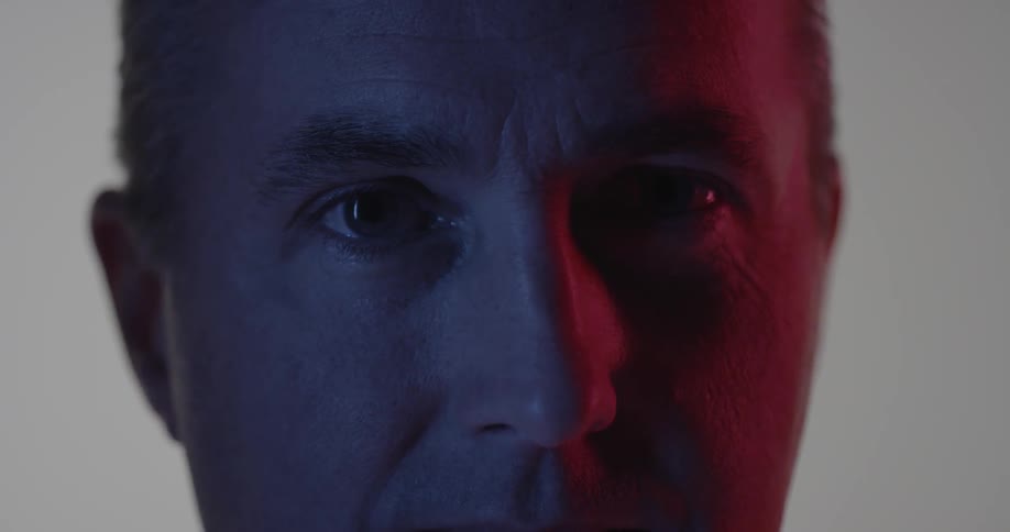 A man stares forward in the dark blinking once