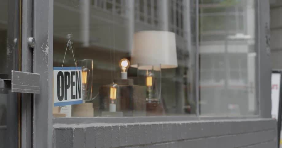 A person turns around a closed shop sign to show it is open