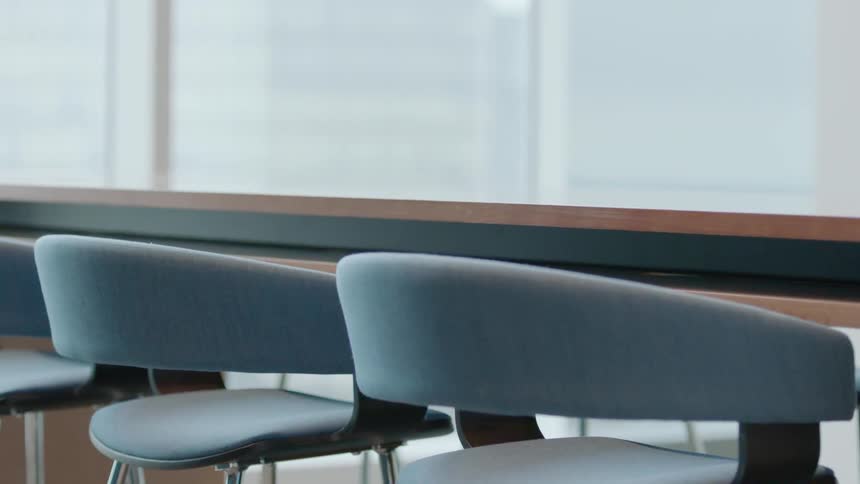 Empty chairs sit pulled up to a conference table in an office during the day