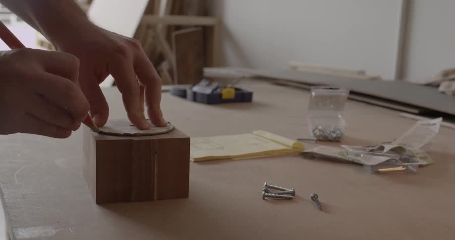 A man traces a circle on a block of wood in a workshop