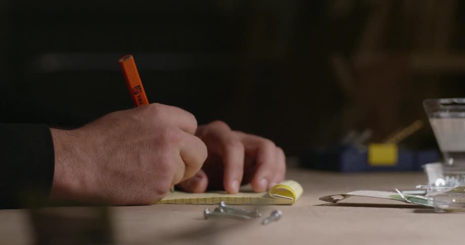 Person writes on a yellow notepad with an orange pencil