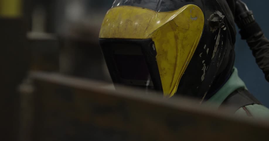 A man wearing a welding mask works on a steel beam