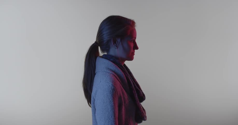 A woman in a jacket stands in front of a white backdrop