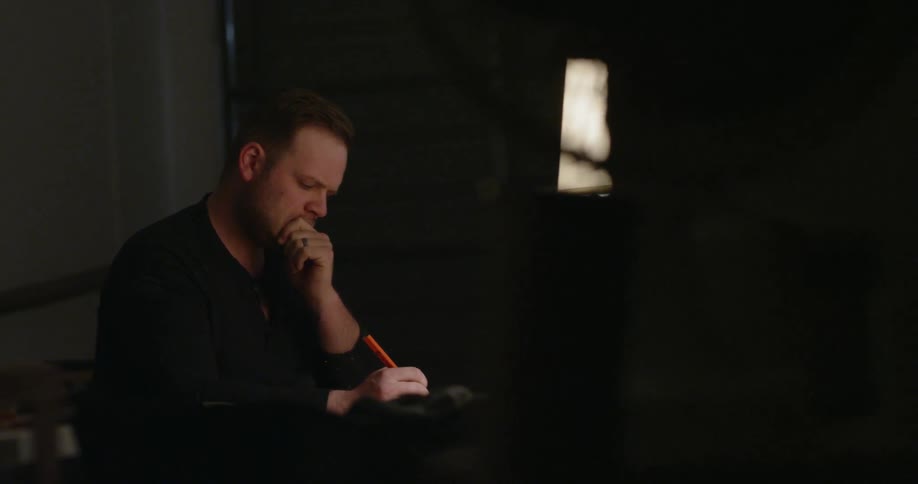 A man is thinking as he prepares to write something down inside at night
