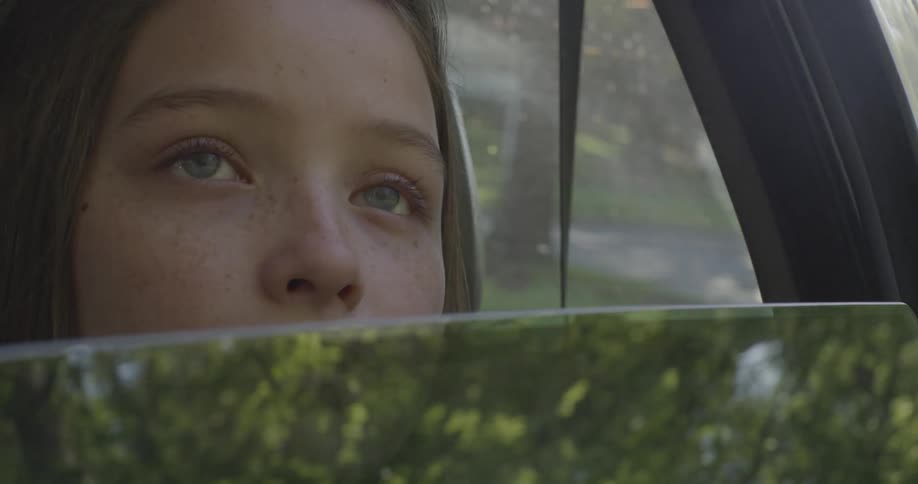 A girl is looking out of the rolled down window of a car as it drives in daylight