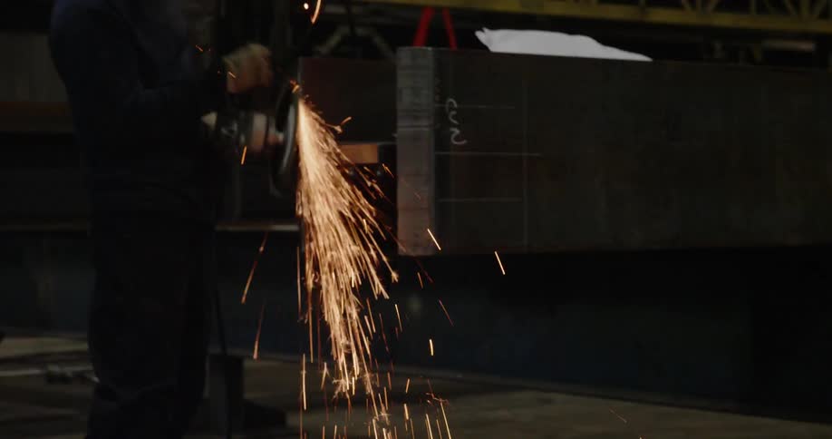 A man grinds a steel beam with a grinder