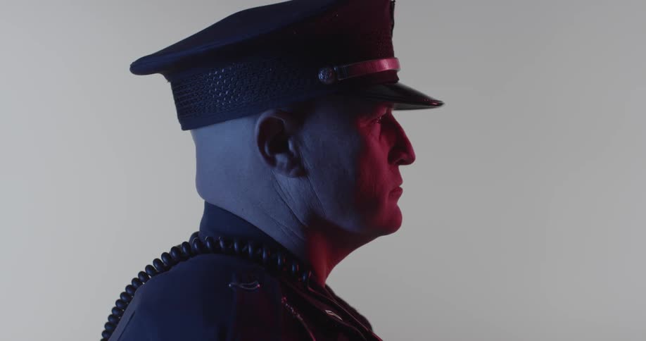 A police officer stares forward in a dim room