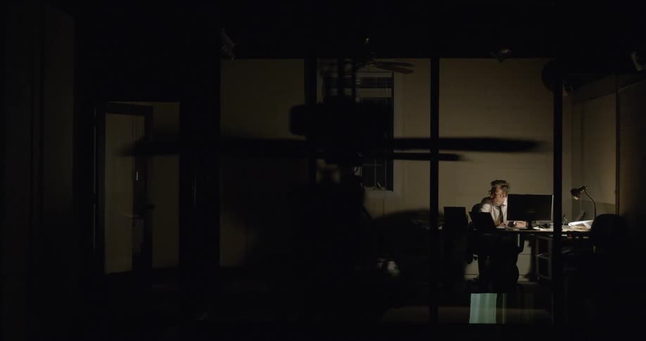 A man is working at a computer in an office at night