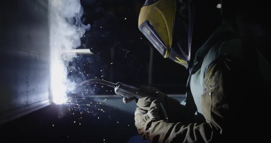A worker is wearing a mask as he uses a welder in the dark