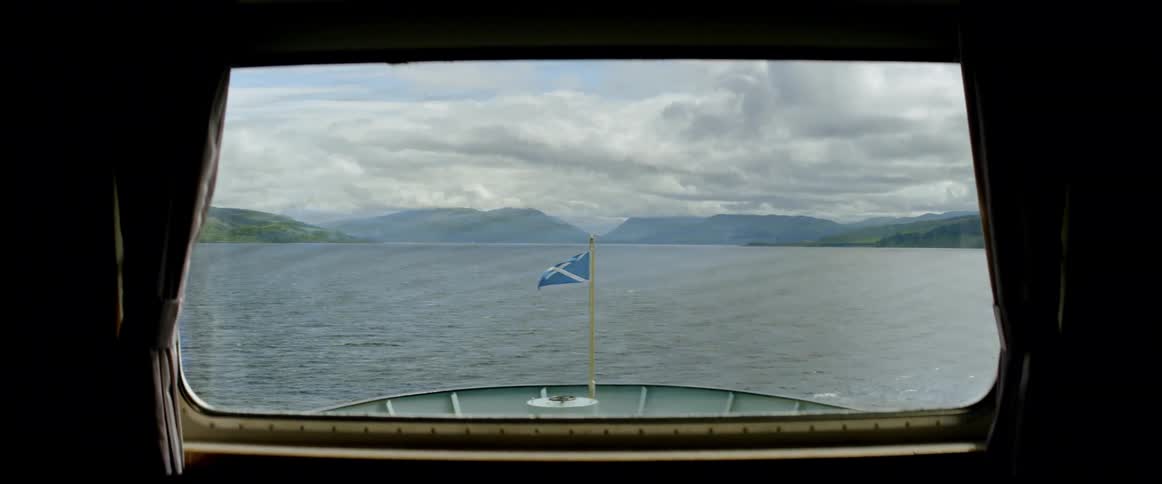 A ship floats on a mountain lake while flying the flag of scotland