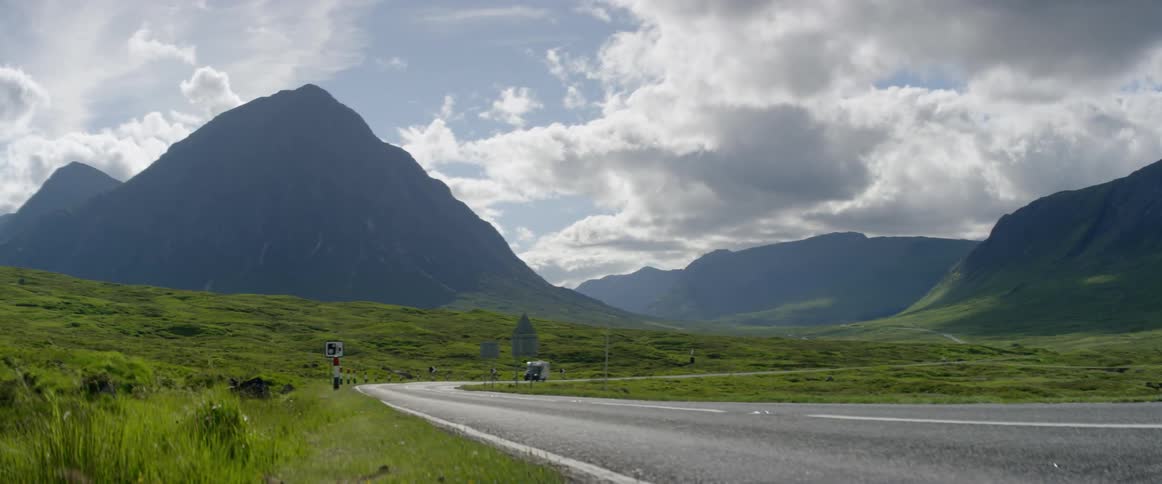 A camper is traveling down a road with a large mountain in the background