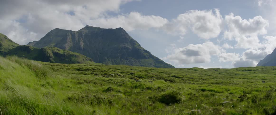 Clouds hover over a mountain and grasslands during the day