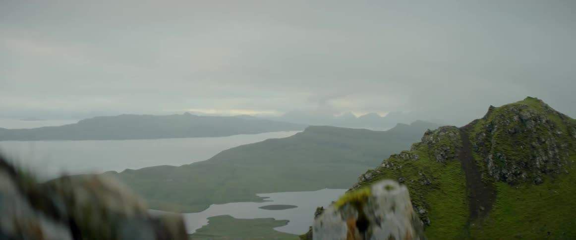 Gray clouds hang over stone mountains and a lake
