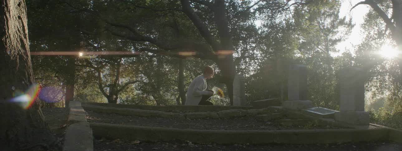 A woman is placing flowers at a gravestone during the day