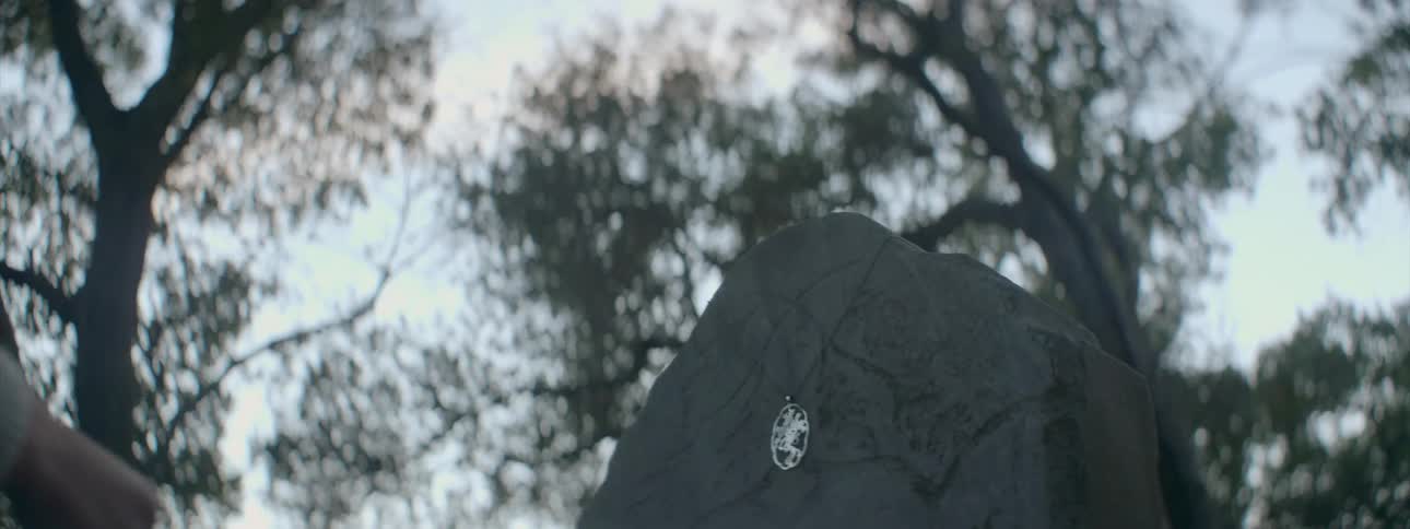 A woman hangs a necklace on a headstone at sunset