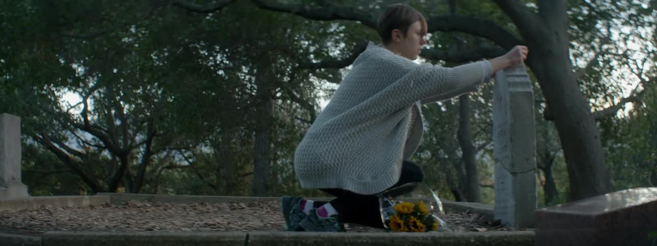 A woman places a necklace on a headstone
