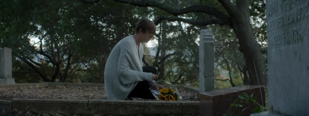 Woman places a bouquet of flowers by a gravestone