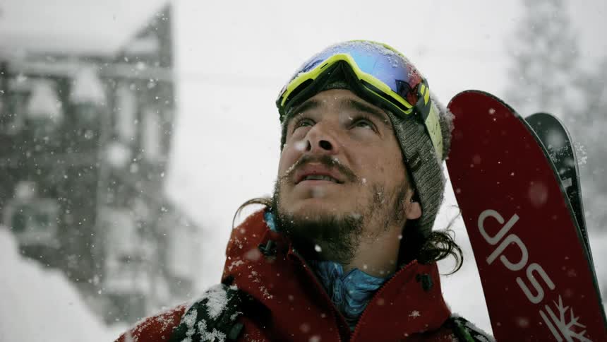 A skier looks up into the sky as it snows