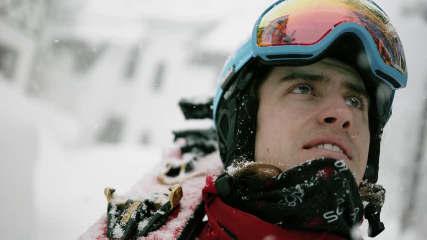 A skier is watching as snow is falling around him outside in daylight
