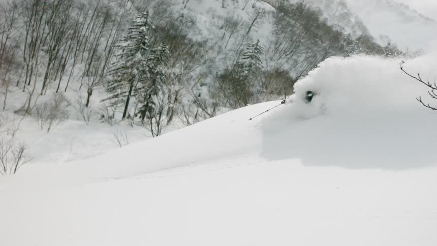 A skier is turning through deep snow as he goes down a hillside in daylight