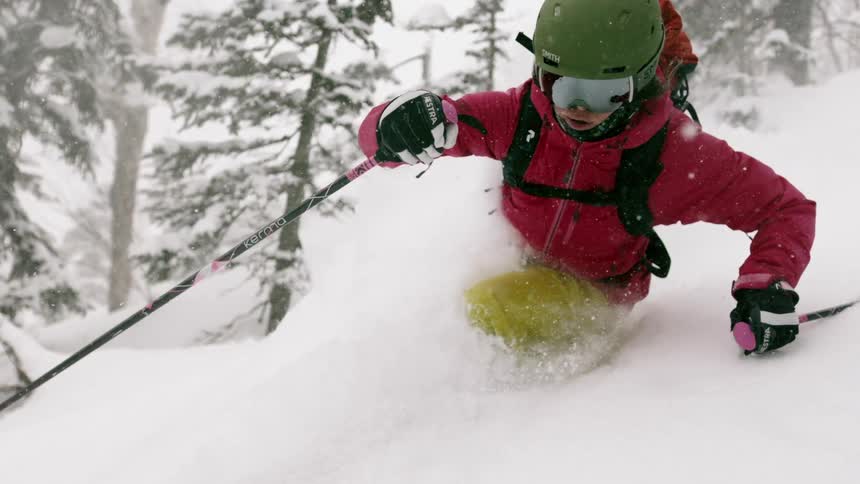 A skier turns through deep snow as she goes down a hillside in daylight