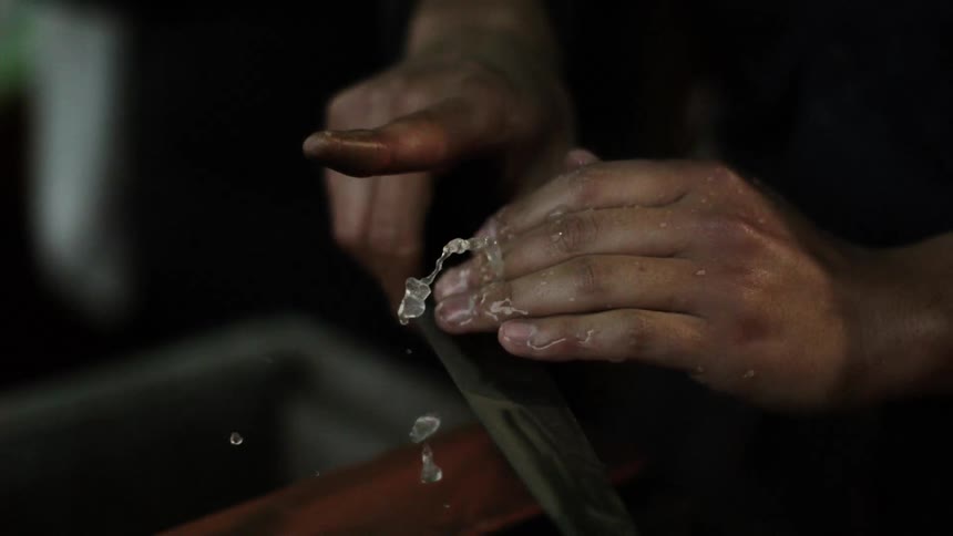 A man is wetting down a blade as he sharpens it in extreme slow motion