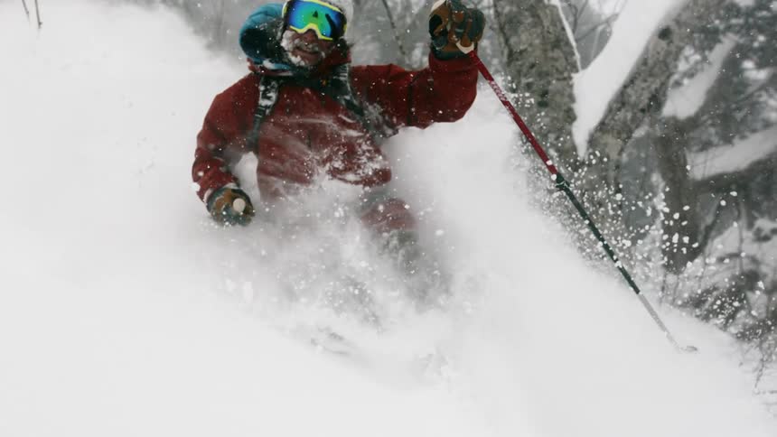 A smiling person skiing downhill through a forest
