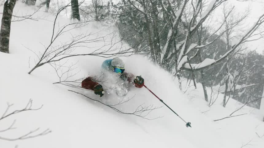 A skier is turning through deep snow as he goes down a hillside in daylight