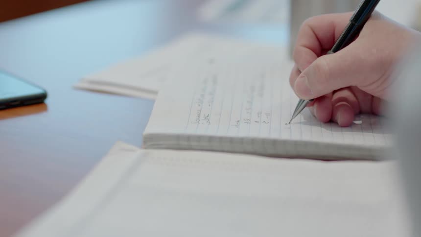 Person writes on a notebook with a pen