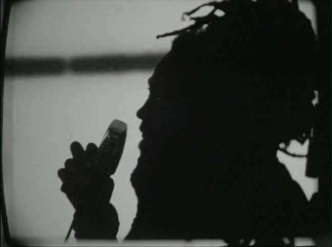 A silhouetted man sings into a microphone with projections on the wall behind him
