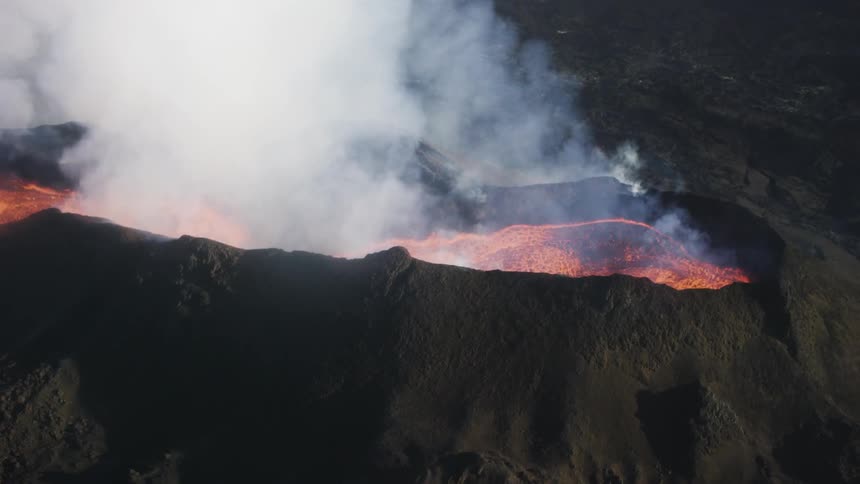 Aerial view of lava bubbling up inside of a volcano and steam rising from the mouth