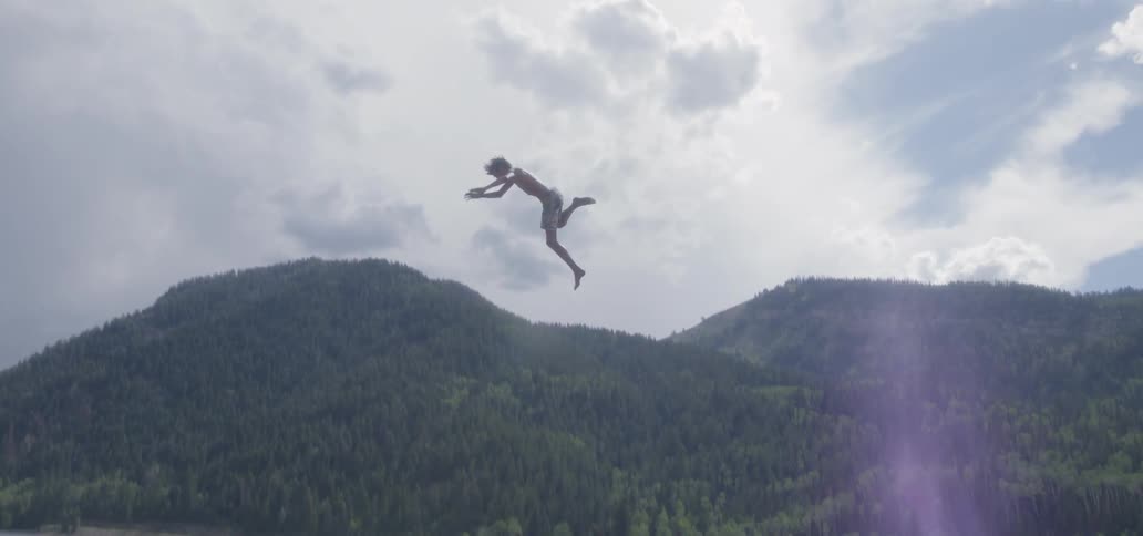 A man swings from a cliff and dives into the water