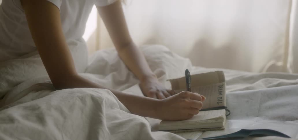 A woman writes in a notebook while sitting in bed