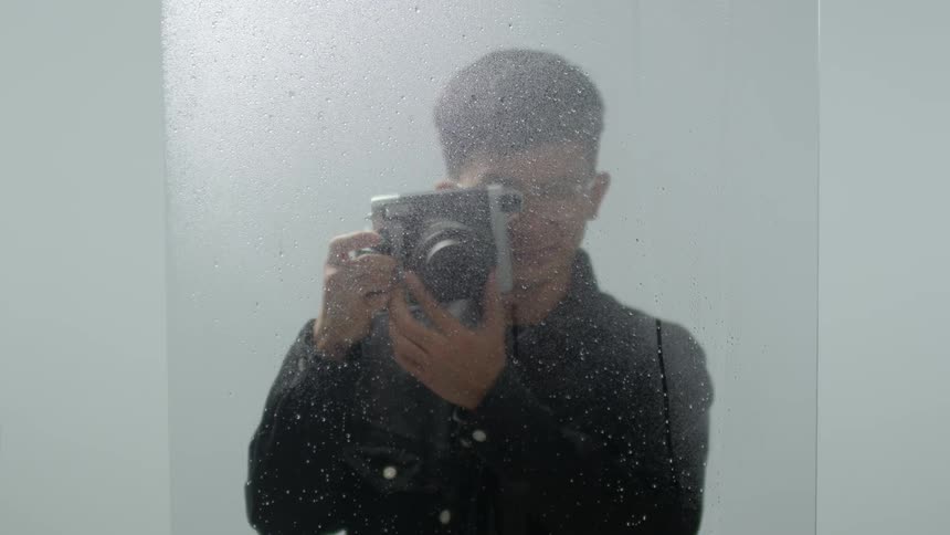 A man adjusts a camera lens and points it towards a piece of glass