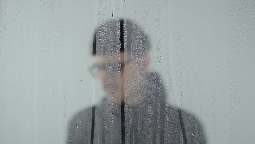 A man stands in front of a wet window