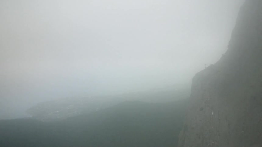 Mist hovers around a rocky cliff